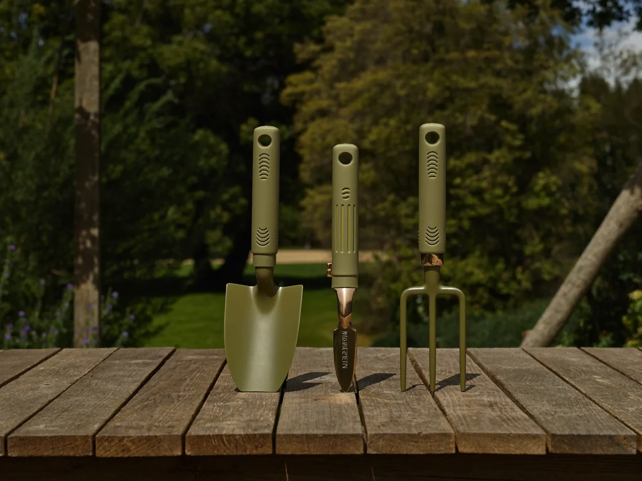 Trapiantatoio, forchetta e cesoie leggeri con impugnature morbide su un tavolo da giardino.