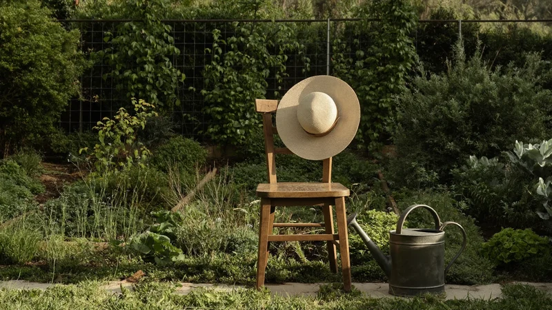 Angolo d'orto ombreggiato con sedia di legno, cappello di paglia e annaffiatoio.